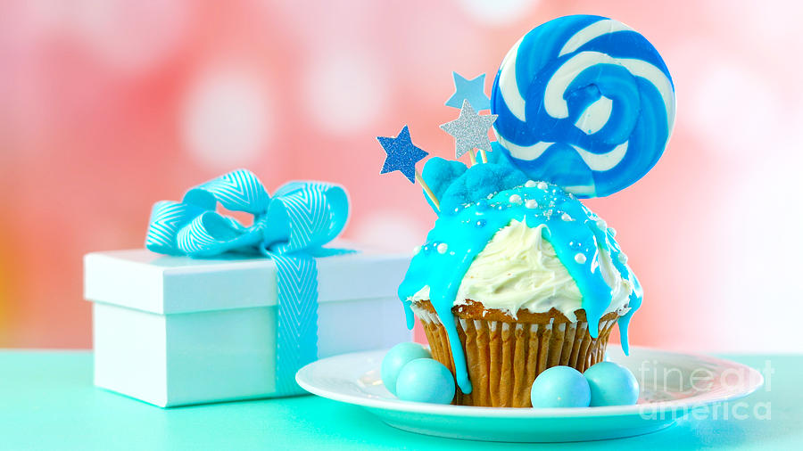Blue novelty cupcake decorated with candy and large lollipops. Photograph by Milleflore Images