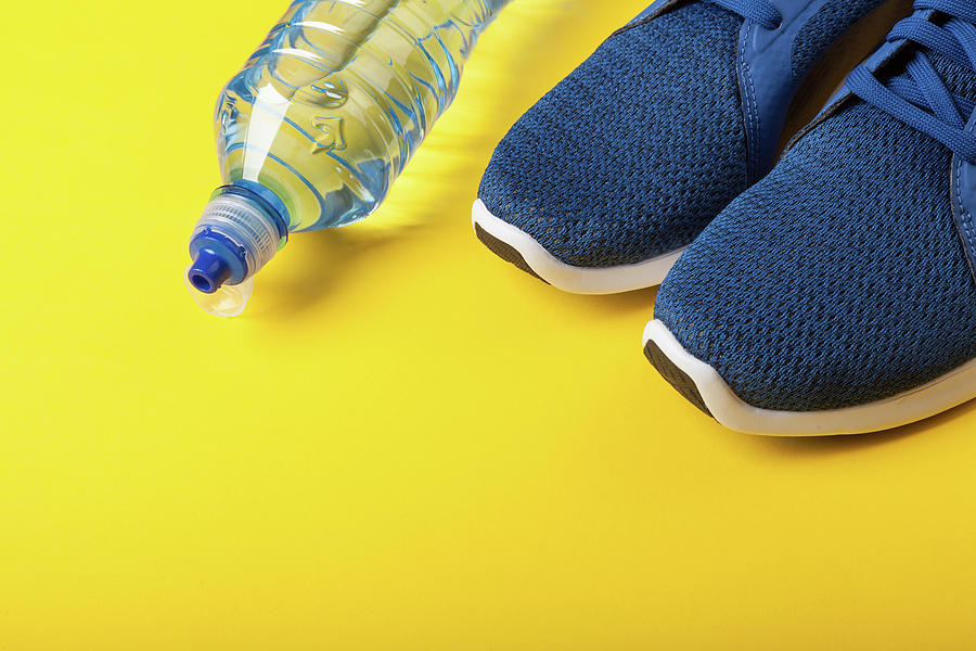 Blue Sneakers And Bottle Of Water On Yellow Background. Concept Of Healthy Lifestile, Everyday Training And Force Of Will Photograph