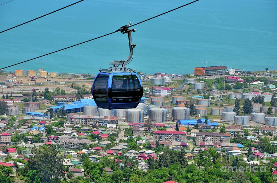 Blue tinted glasses cable car moves over green forest area and city buildings Batumi Georgia Photograph by Imran Ahmed