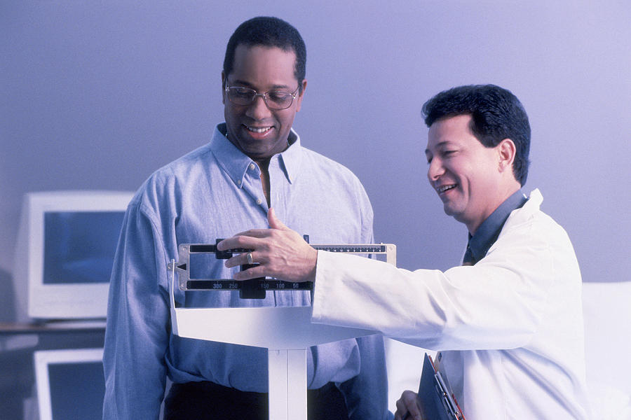 Blue tone of a doctor weighing a male patient Photograph by Thinkstock