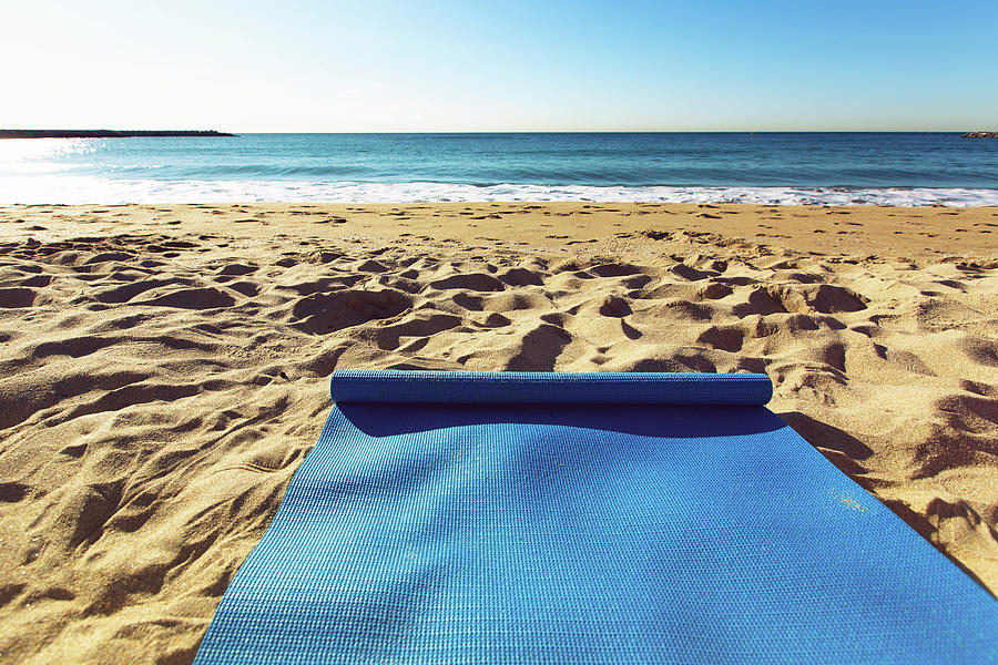 Blue yoga mat is on a sandy beach by the sea. Barcelona, Spain by Anna  Finist