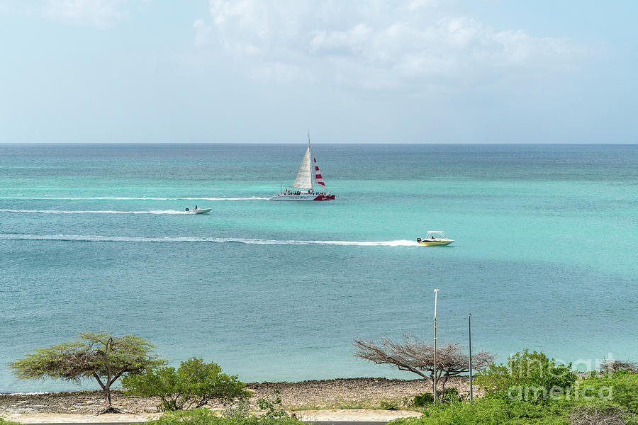 Boats cruise past the shore near Eagle Beach on the Caribbean is Photograph by William Kuta