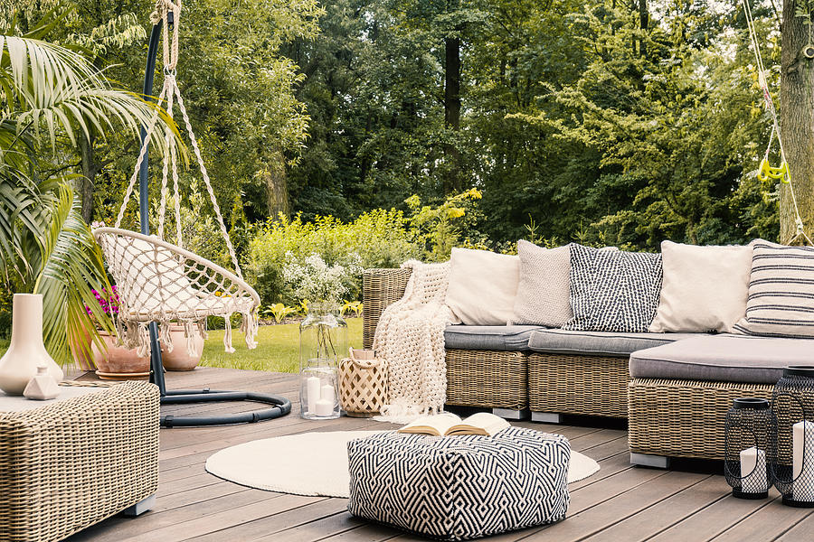 Book on a black and white pouf in the middle of a bright terrace with a rattan corner sofa, hanging chair and round rug. Real photo Photograph by KatarzynaBialasiewicz