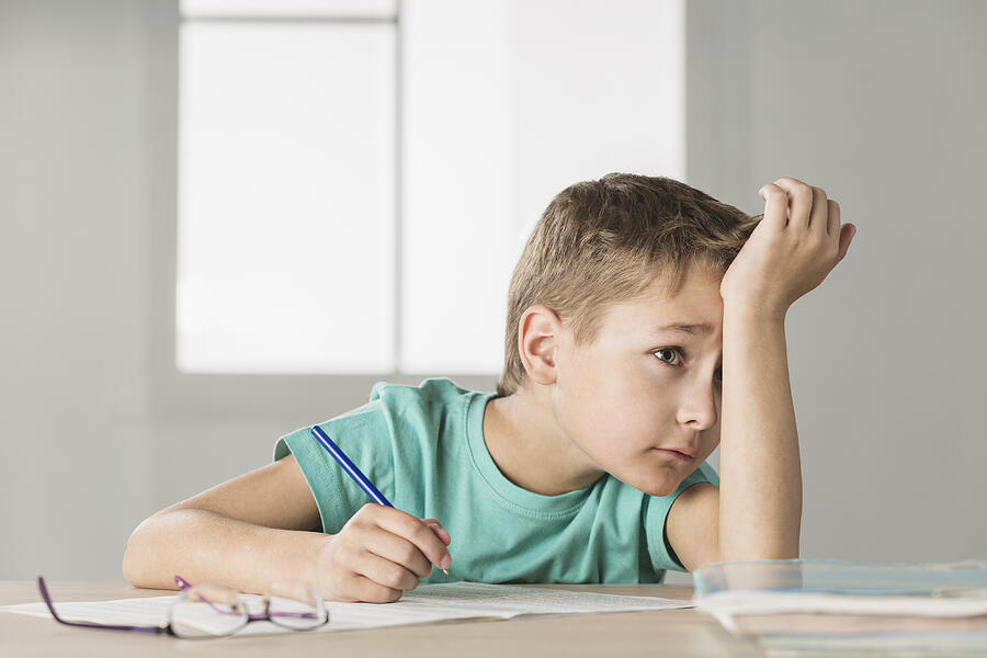 Bored boy with hand on forehead doing homework at home Photograph by Vladimir Godnik