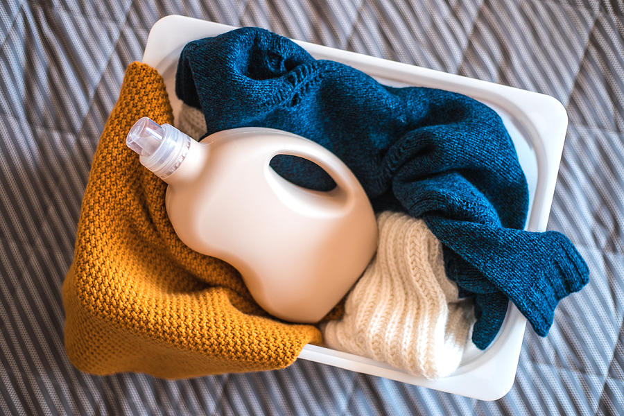 Bottle of detergent with sweaters in container. Photograph by Evgeniia Siiankovskaia