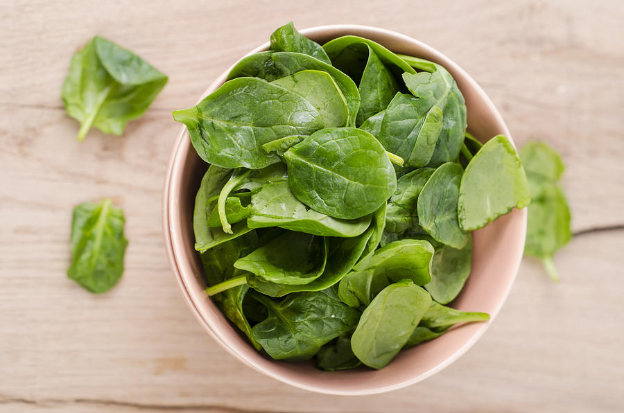 Bowl of fresh spinach leaves on wood Photograph by Westend61