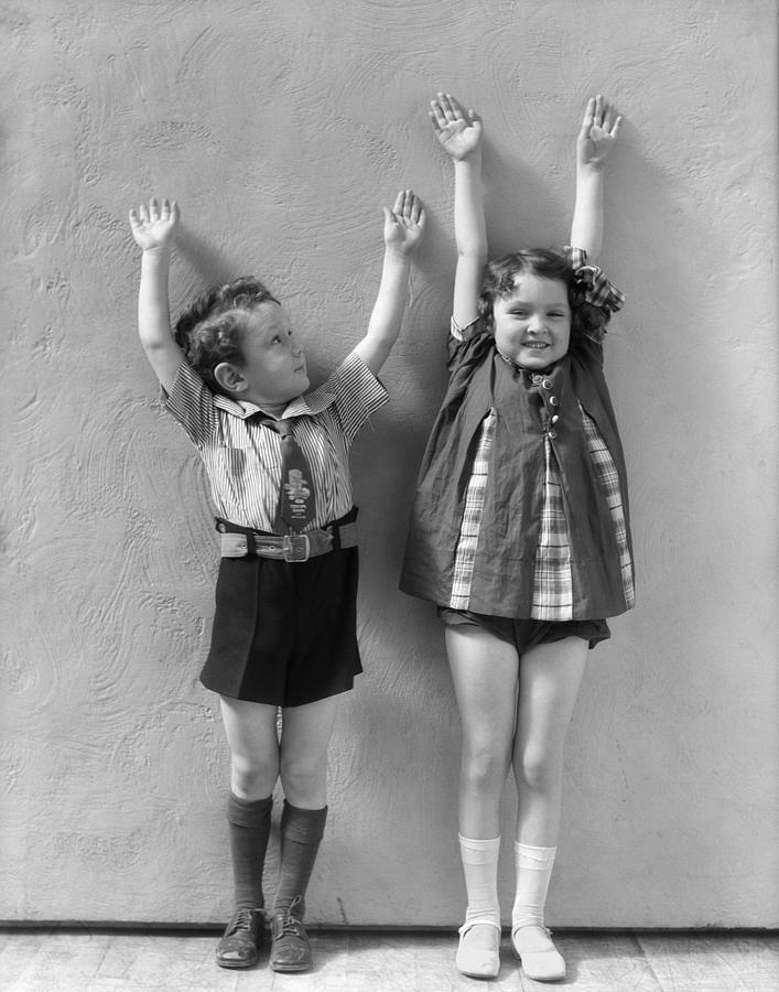 Boy & Girl Standing Next To One Another With Arms Raised Above There Heads Girl Is Wearing A Panel Dress And White Socks & Shoes Boy Shirt Tie Shorts. Photograph by H. Armstrong Roberts