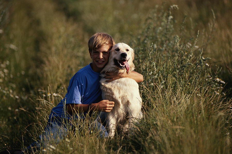 Boy (10-12) embracing dog in field Photograph by David De Lossy