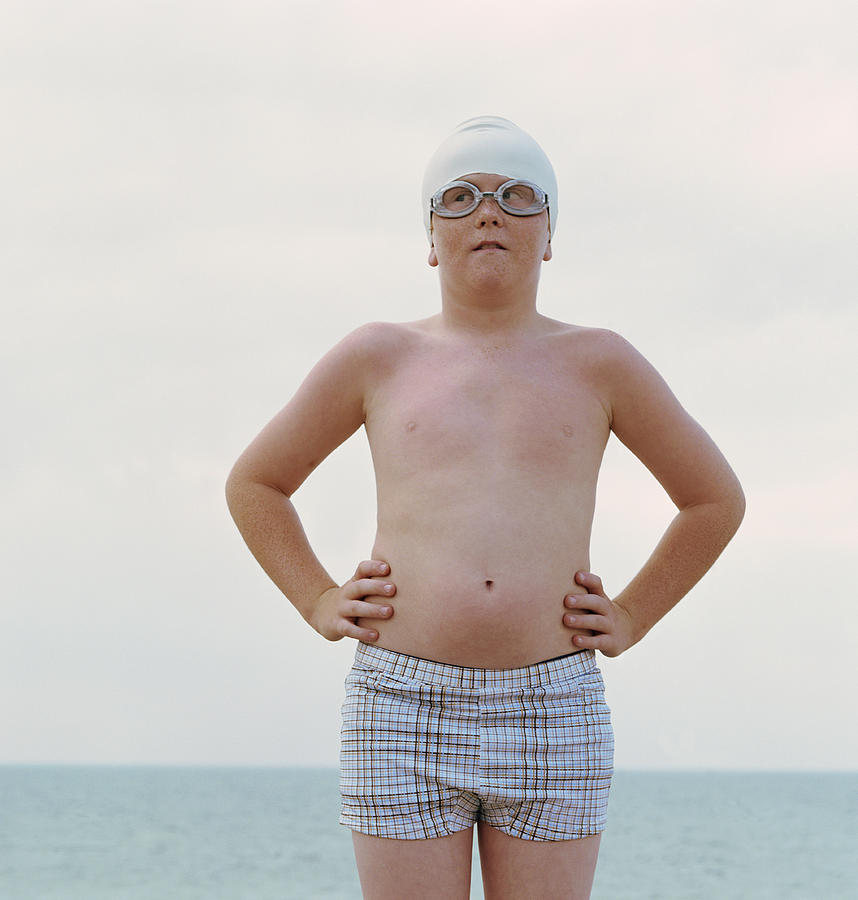 Boy (10-12) wearing swimming cap and goggles, hands on hips Photograph by Marcelo Santos