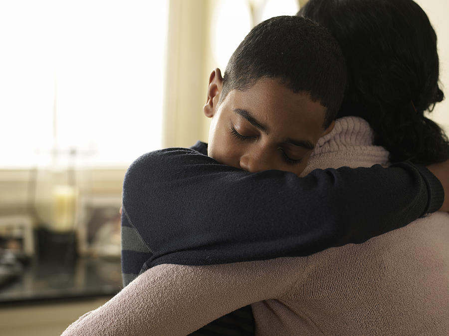Boy (12-13) hugging mother at home Photograph by John Howard