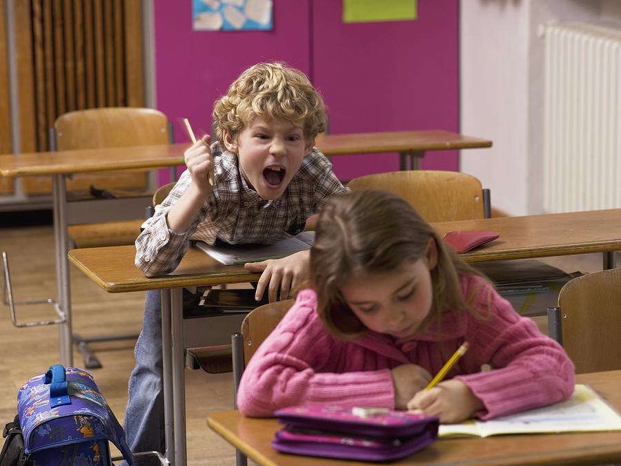 Boy (4-7) shouting behind girl in class room Photograph by Westend61