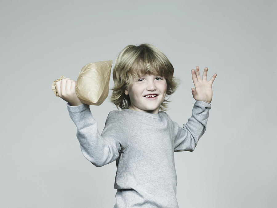 Boy (6-7) bursting paper bag, smiling, portrait Photograph by Flashpop