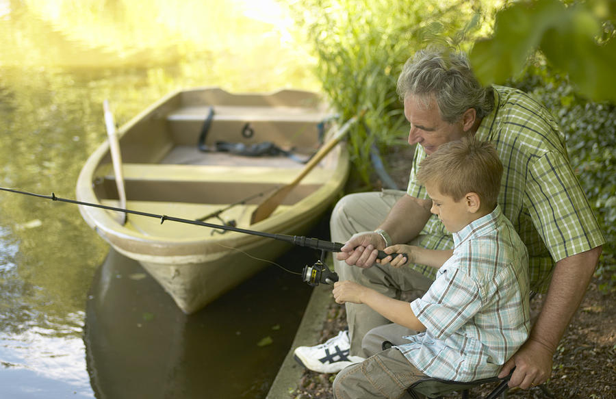 Boy (6-8) and grandfather fishing from side of lake Photograph by Jochen Sand
