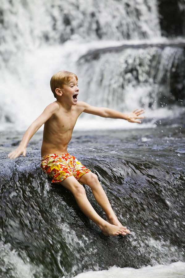 Boy (6-8) sliding down waterfall, arms outstretched Photograph by Phillip Spears