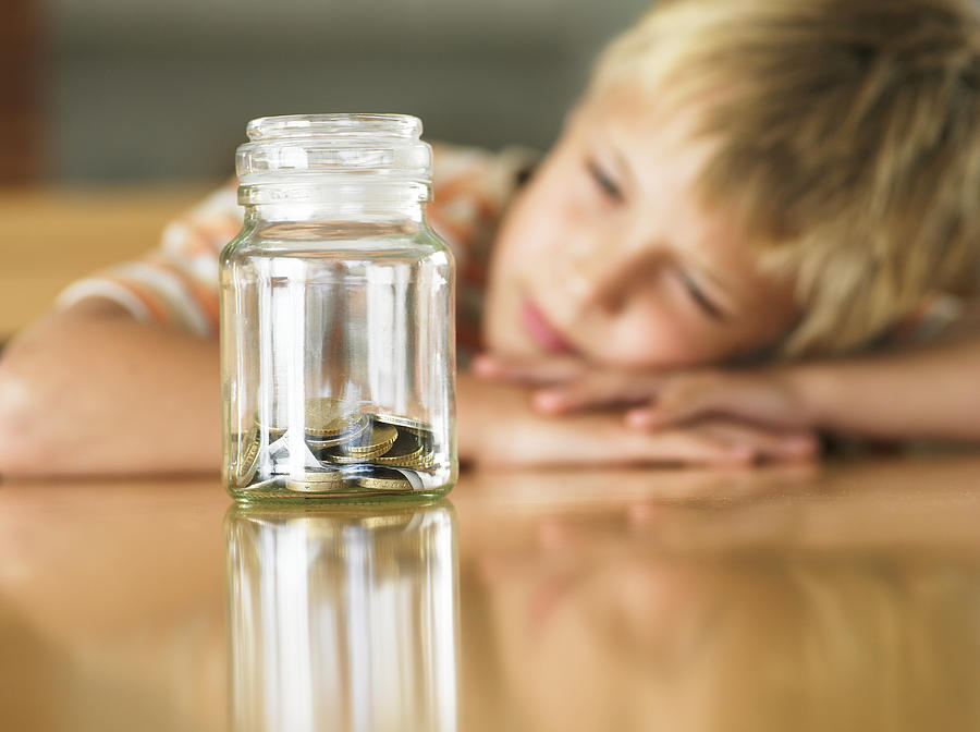 Boy (7-9) looking at coins in jar (focus on jar) Photograph by Flying Colours Ltd