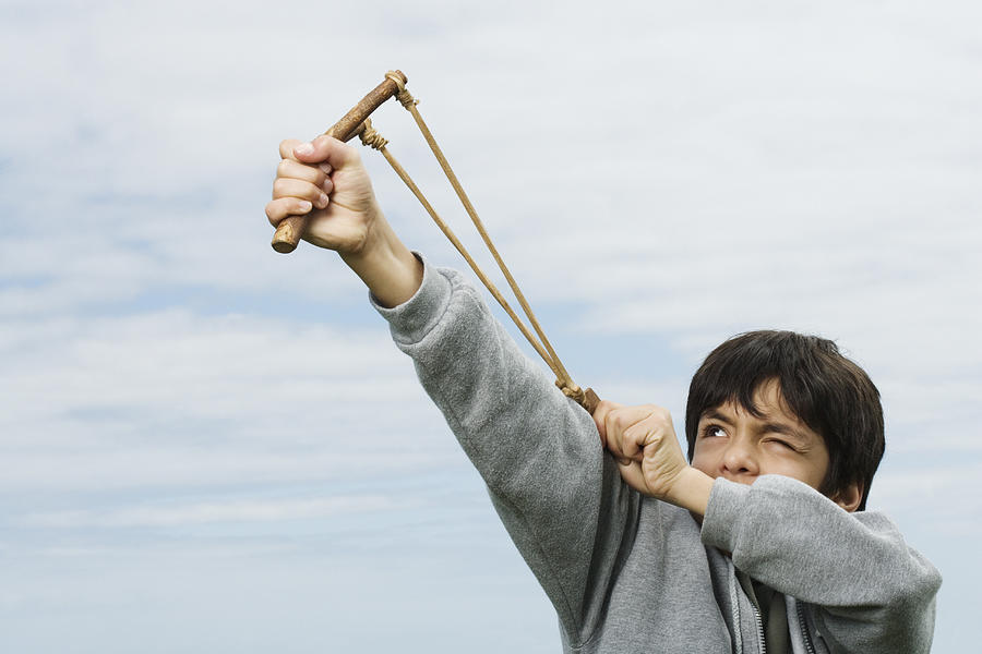 Boy (8-10) shooting catapult, one eye closed Photograph by Tay Rees