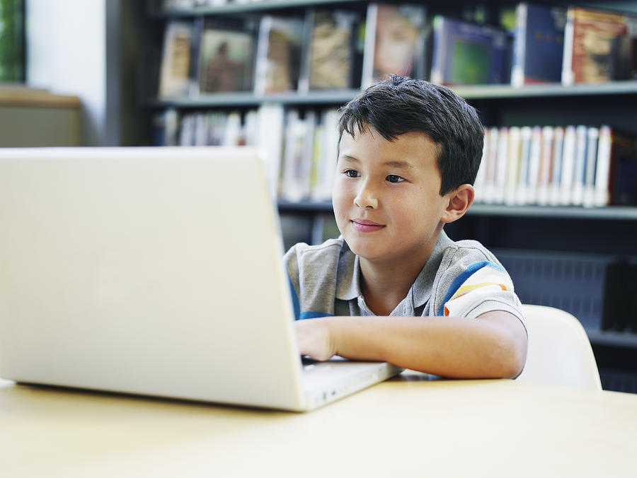 Boy (8-10) using laptop in library, smiling Photograph by Thomas Barwick