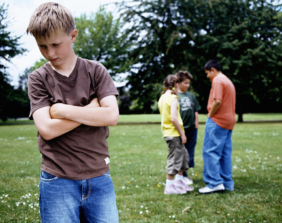 Boy (9-11) standing in park, arms crossed, group (10-12) in background Photograph by Digital Vision