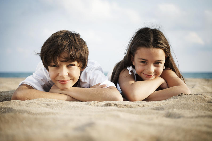Boy and girl (8-10) lying on beach, smiling, close-up, portrait Photograph by Getty Images