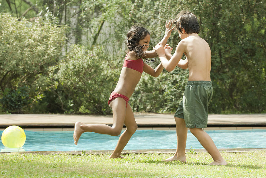 Boy and girl playfighting at poolside Photograph by Odilon Dimier/PhotoAlto