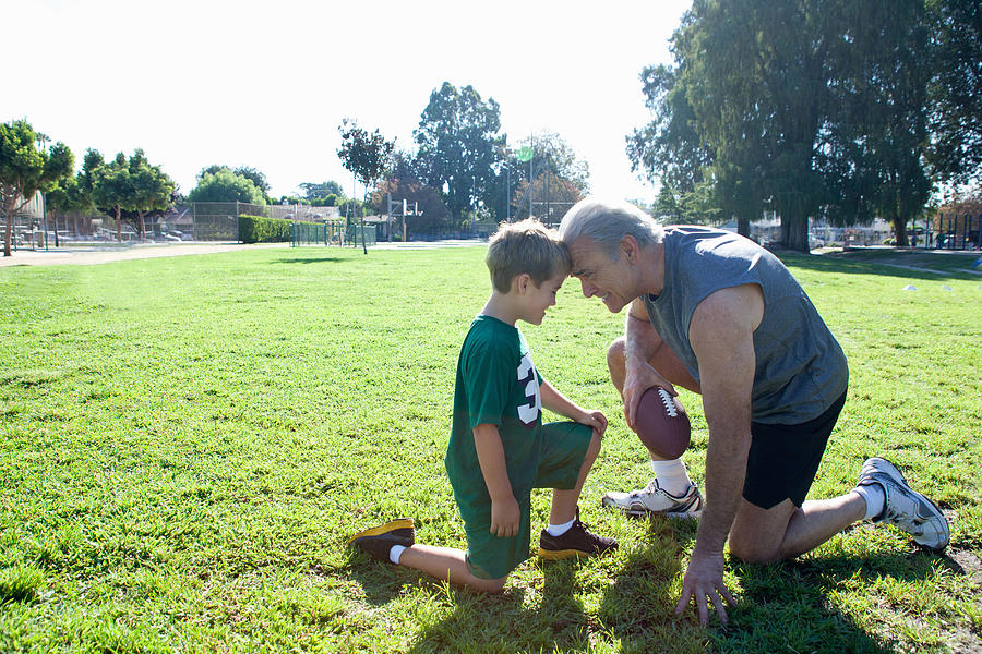 Boy and grandfather head to head, man holding football Photograph by David Jakle