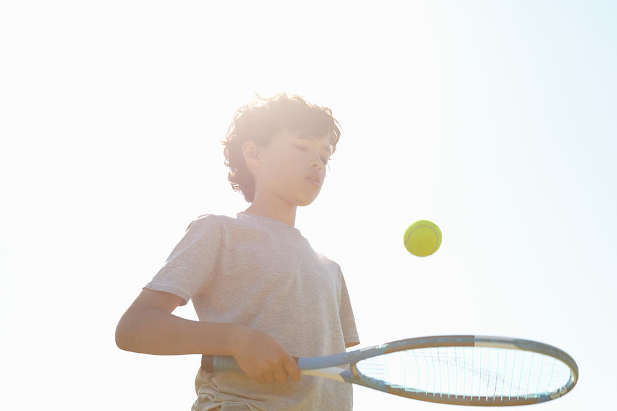 Boy bouncing ball on tennis racket Photograph by Emma Kim