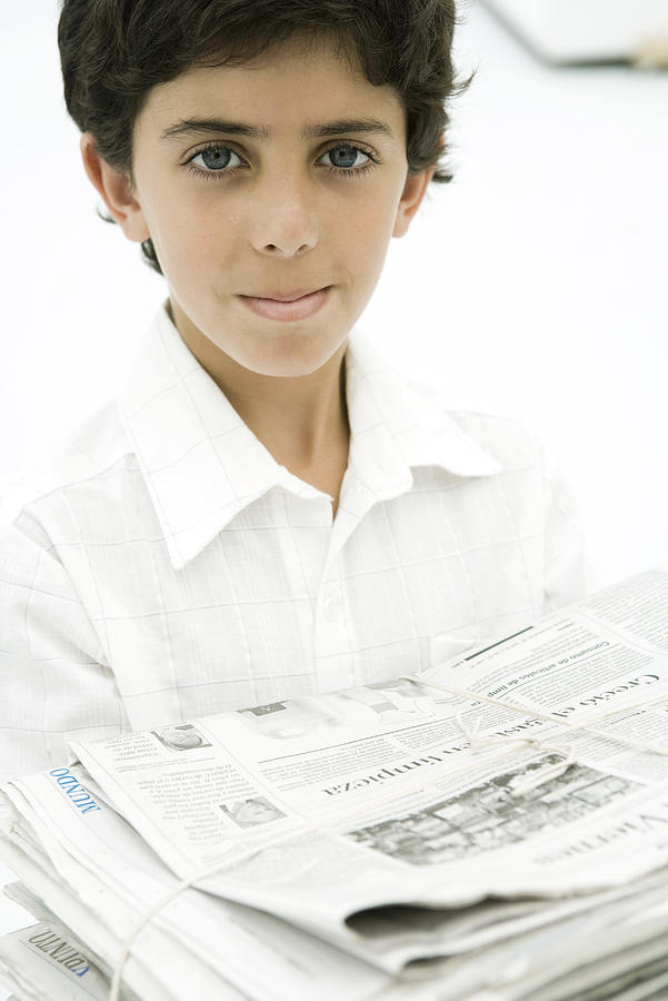 Boy carrying stack of newspapers, smiling at camera Photograph by PhotoAlto/Sigrid Olsson