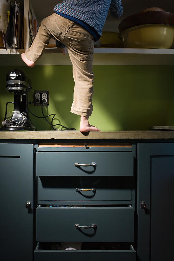 Boy climbing in kitchen Photograph by Image Source