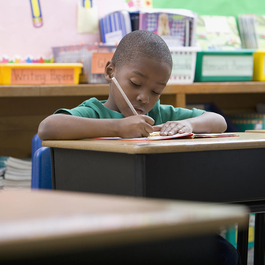 Boy doing school work at desk in classroom Photograph by Wealan Pollard