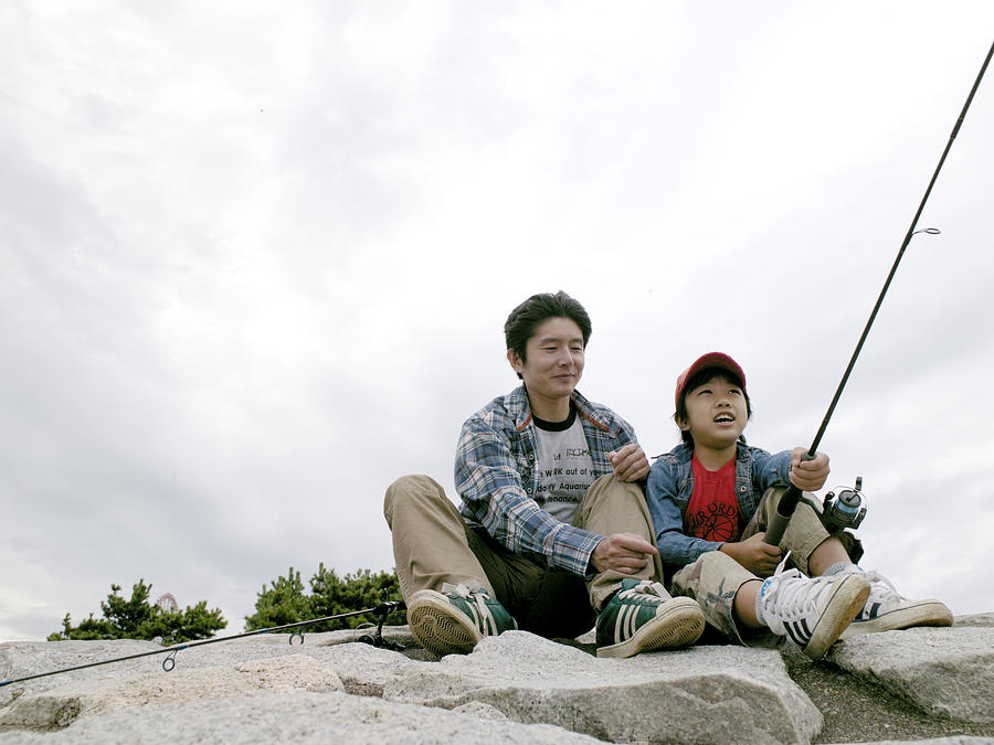 Boy holding a fishing rod with his father beside him Photograph by Dex Image