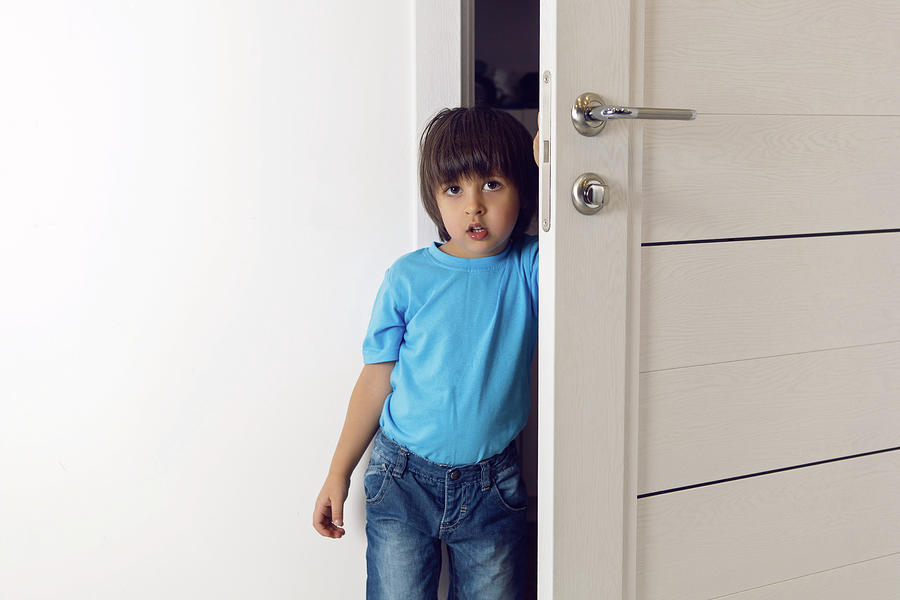 boy in a blue T-shirt and jeans is standing at home in the white door ...