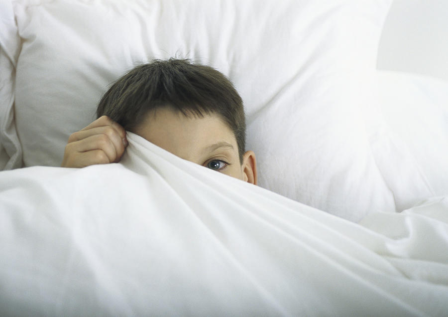 Boy in bed, peeking out behind sheet with one eye Photograph by Sigrid Olsson