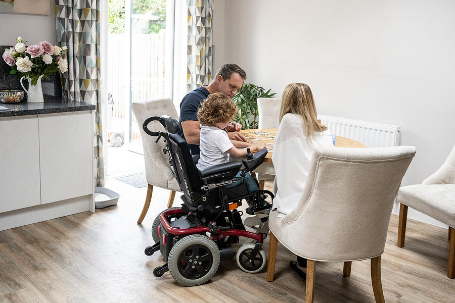 Boy in wheelchair doing jigsaw with parents Photograph by JohnnyGreig