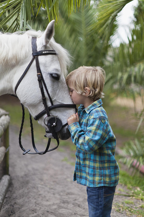 Boy kissing horse in yard Photograph by Hybrid Images