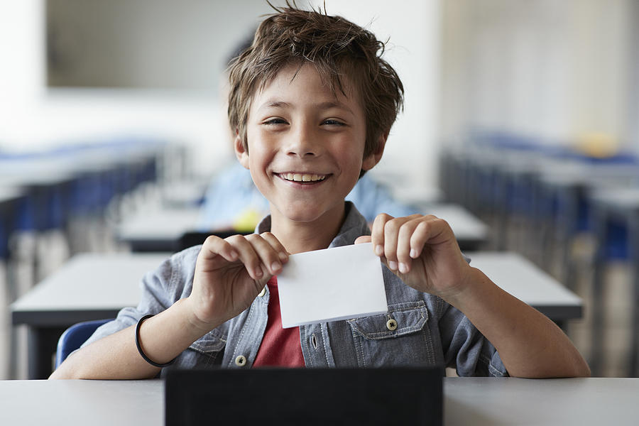Boy laughing and holding paper note, sitting in classroom Photograph by Klaus Vedfelt