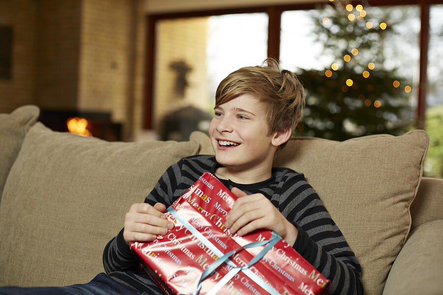 Boy laughing in sofa holding present Photograph by Klaus Vedfelt