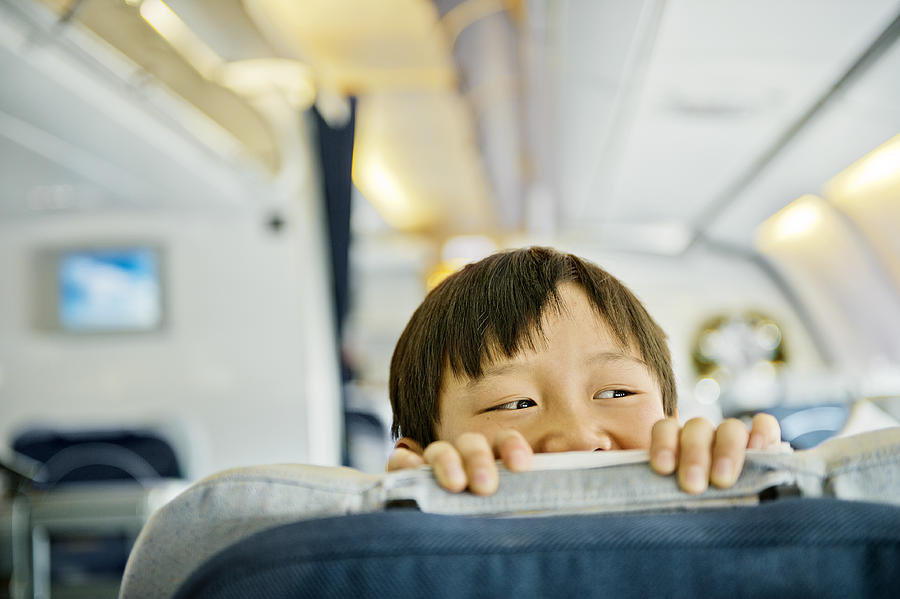 Boy looking over business class seat of plane Photograph by Elisabeth Schmitt