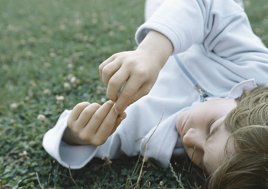 Boy lying on grass holding fingers together in front of face Photograph by Laurence Mouton