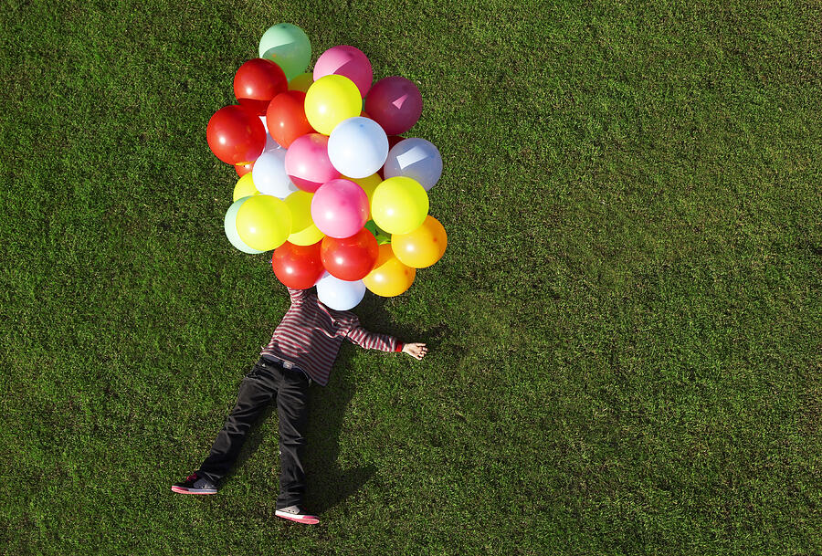 Boy lying on grass with balloons Photograph by Nick Bowers