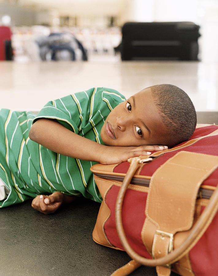 Boy Lying on Luggage on an Airport Baggage Conveyor Belt Photograph by Digital Vision.