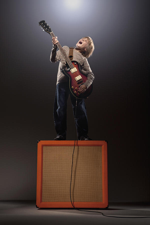 Boy playing electric guitar standing on speaker Photograph by Simon Webb & Duncan Nicholls