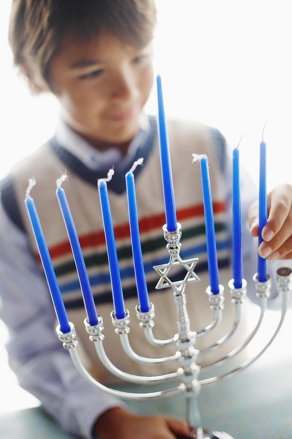 Boy Putting Candle in Menorah Photograph by Fuse