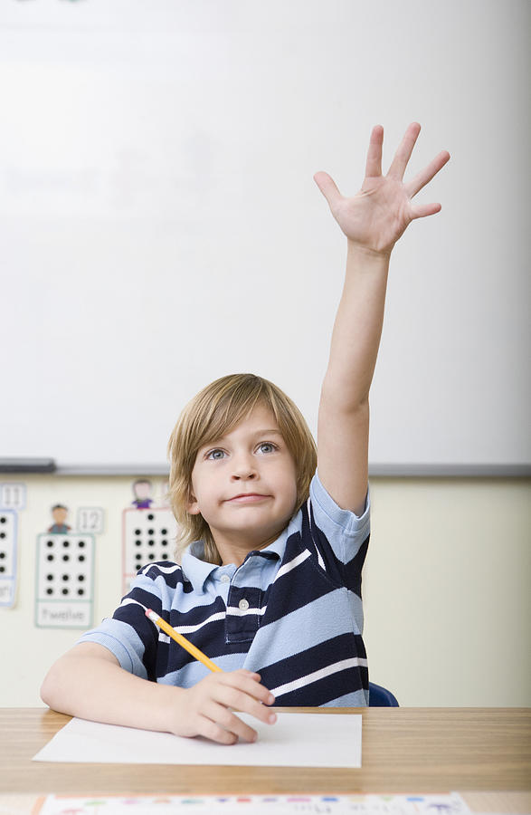 Boy raising hand in classroom Photograph by Wealan Pollard