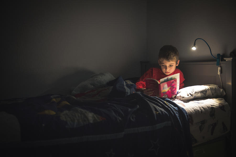 Boy reading in bed with reading lamp Photograph by Teresa Short