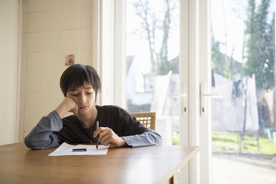 Boy sitting at table, holding pen to paper Photograph by Kaori Ando