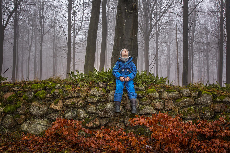 Boy sitting on stone wall in misty forest Photograph by David Trood