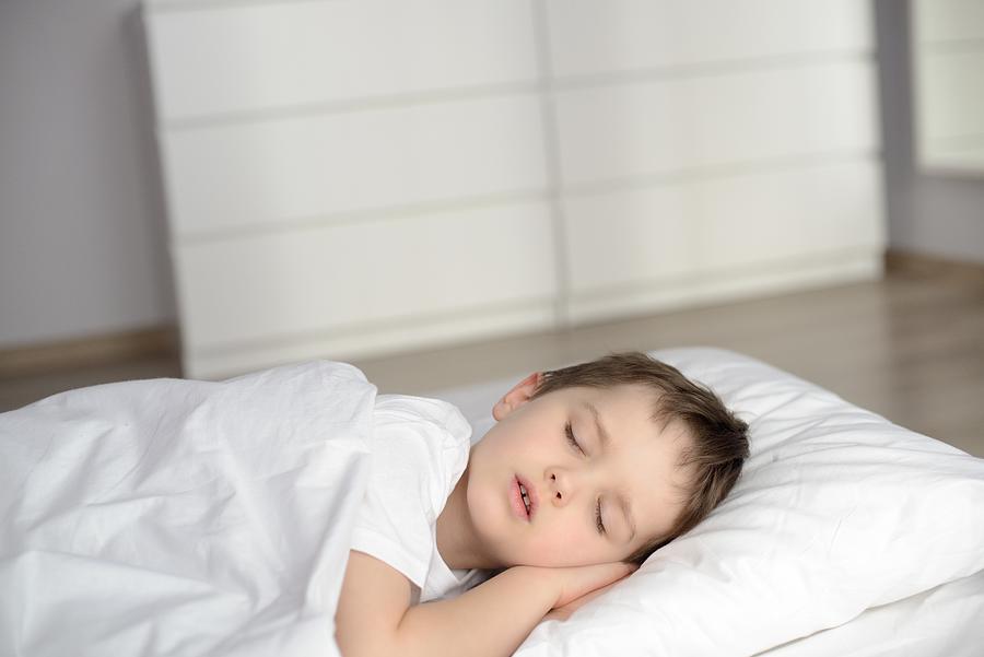 Boy sleeping in bed, happy bedtime in white bedroom Photograph by Djedzura