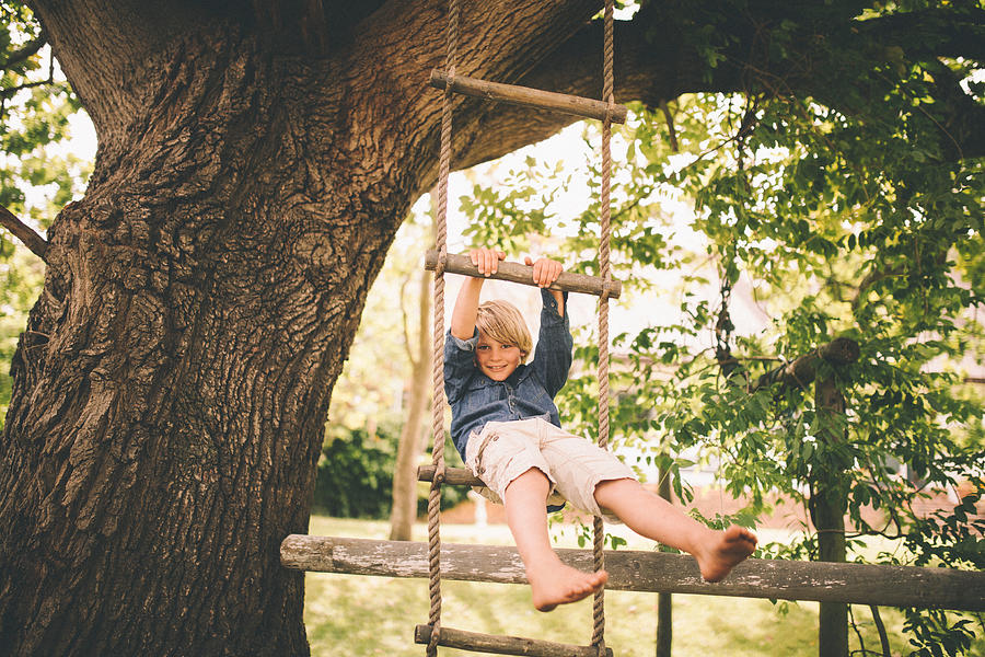 Boy swinging in a rope ladder from tree in park Photograph by Wundervisuals