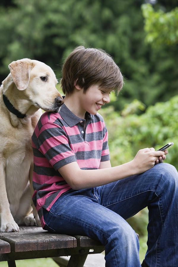 Boy texting, dog looking over shoulder Photograph by Compassionate Eye Foundation/Jetta Productions