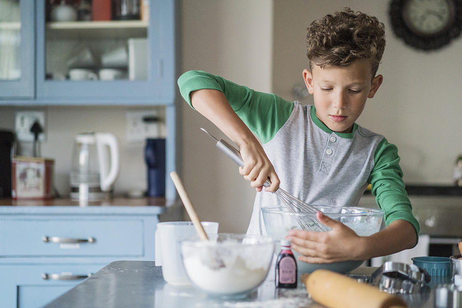 Boy whisking batter in bowl at kitchen counter Photograph by Portra